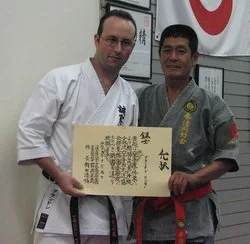 Two men in martial arts uniforms holding a large certificate or award certificate.