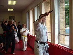 Group of people, including martial artists in traditional uniforms, practicing martial arts in a room with large window and natural light.