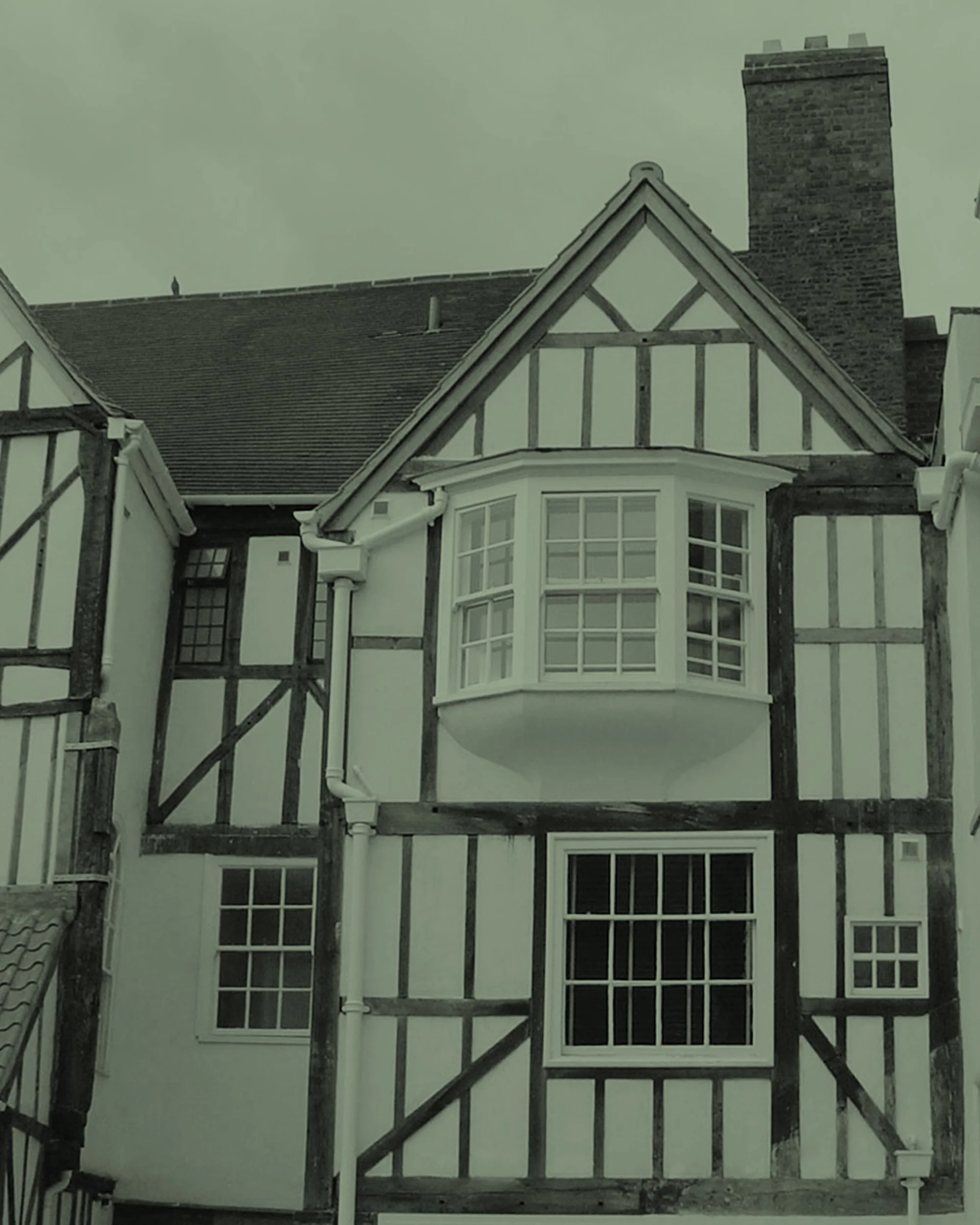 Partial view of a house under renovation with exposed wooden framing surrounding white windows and a chimney in the background.