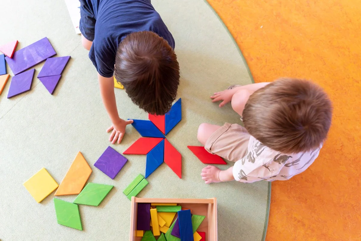Zwei Kinder spielen mit bunten Bauklötzen auf einem Teppichboden.