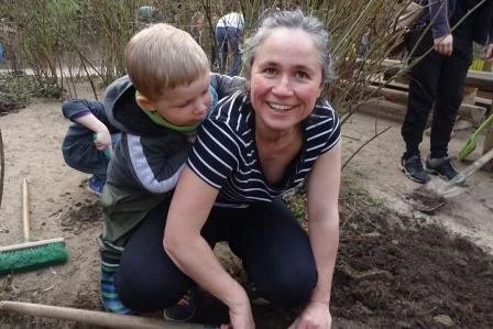 Eine Frau und ein Kind beim Gärtnern im Garten, sie lächeln und sind im Freien.