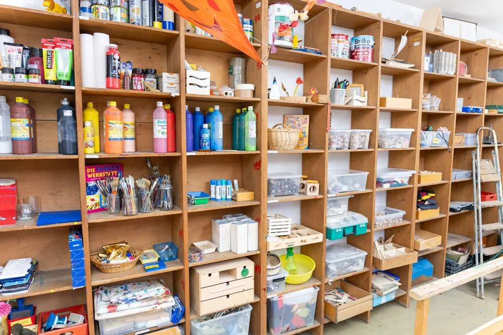 Bücherschrank mit Bastelmaterialien und Farben in einem Bastelraum.