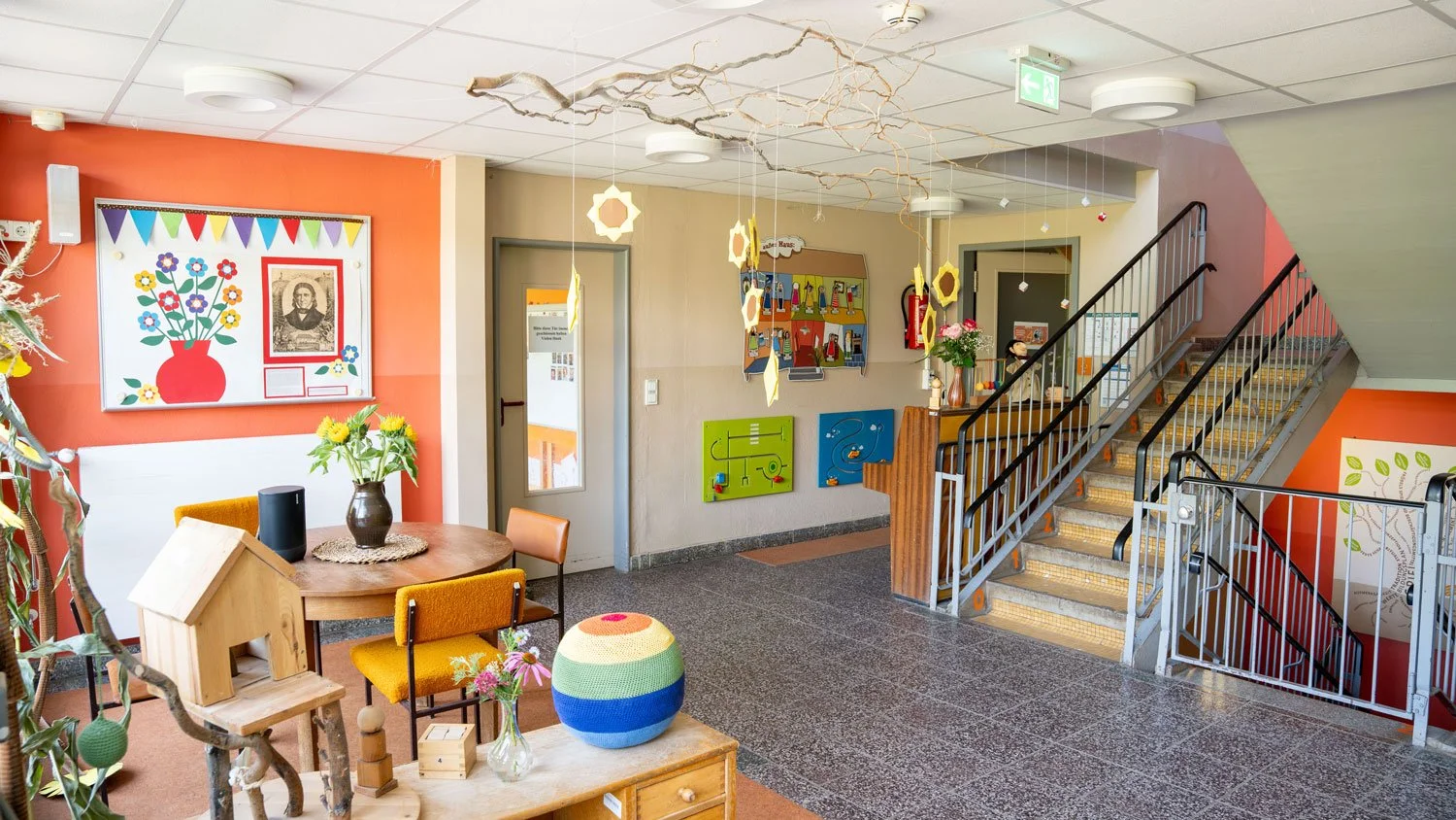 Innenaufnahme eines bunten, kindgerechten Raumes mit Sitzmöbeln, Wanddekorationen, Treppe und Spielzeug.