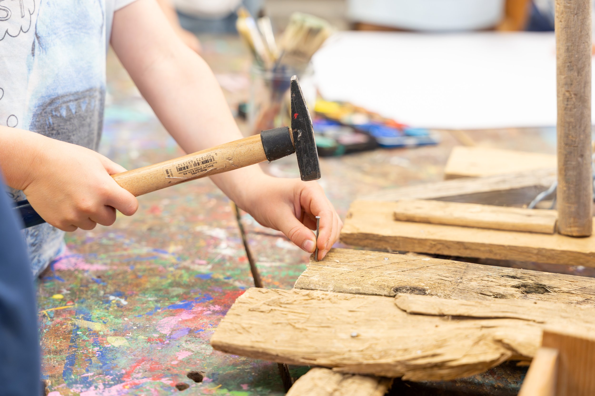 Kind schlagt mit Hammer in Holzstück, kreative Bastelarbeit in Kunstwerkstatt.