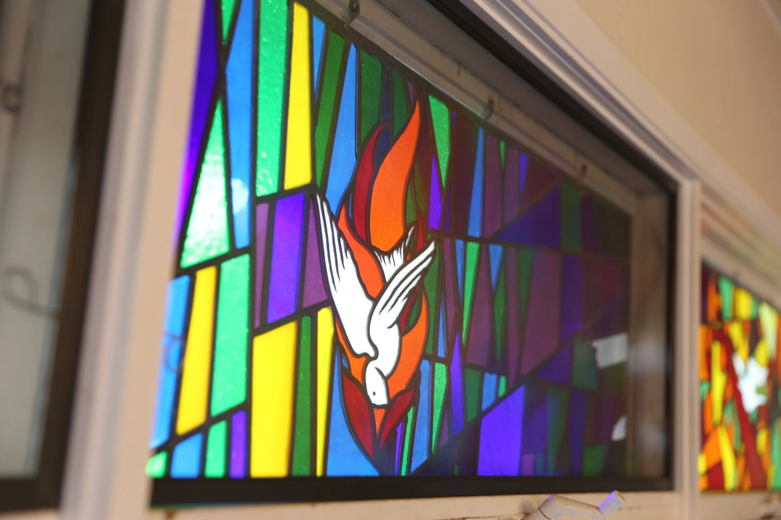Close-up of stained glass window featuring a stylized figure with white and orange robes, framed by colorful geometric shapes.