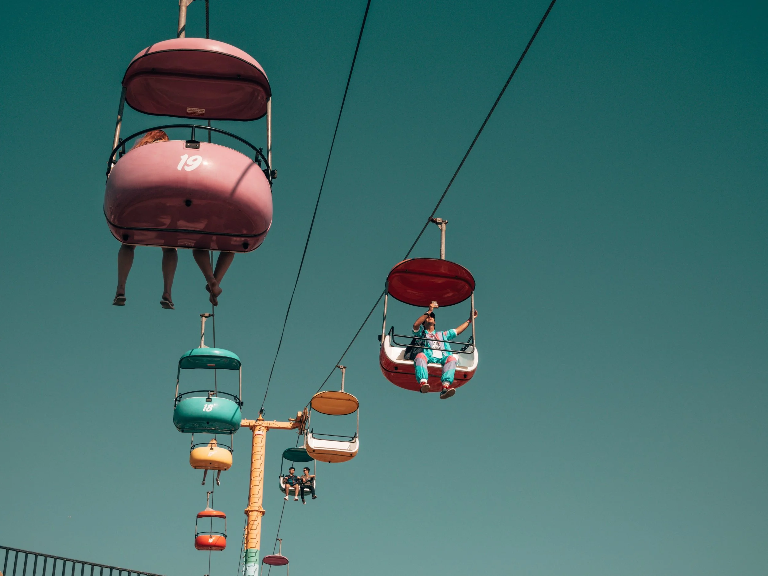 Colorful amusement park Ferris wheel with numbered cabins, blue sky background, and two people sitting in one cabin.