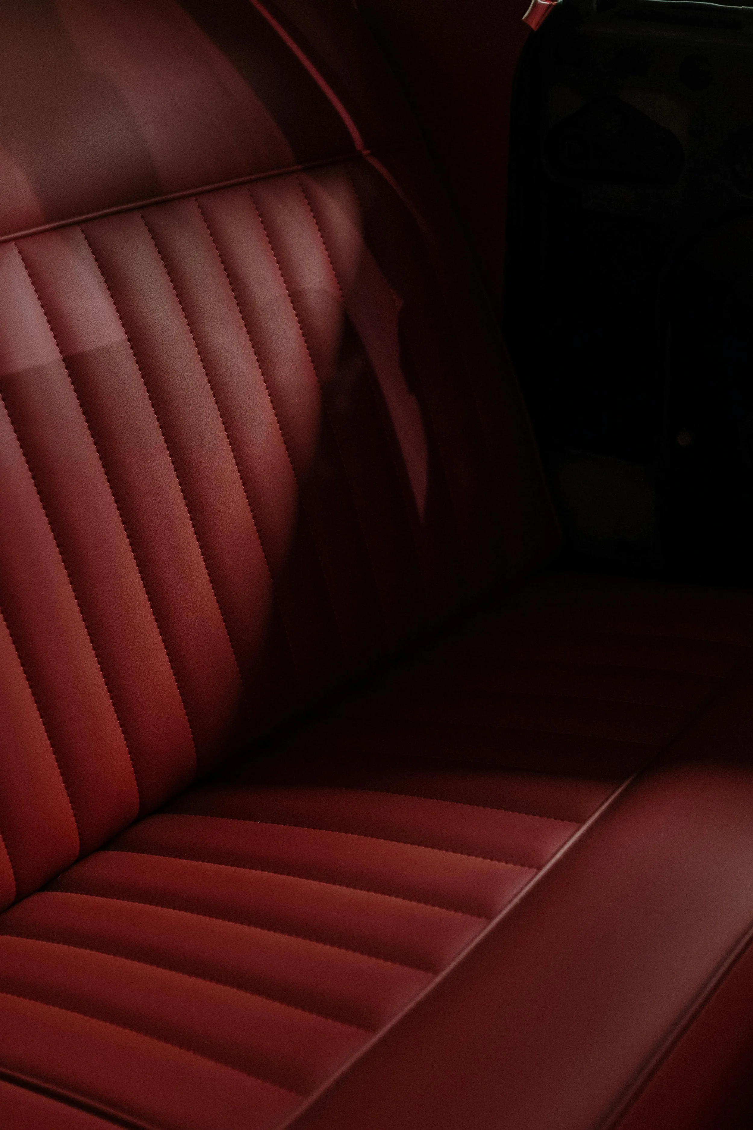 Close-up of the interior of a vintage car, showing red leather seats with vertical stitching.