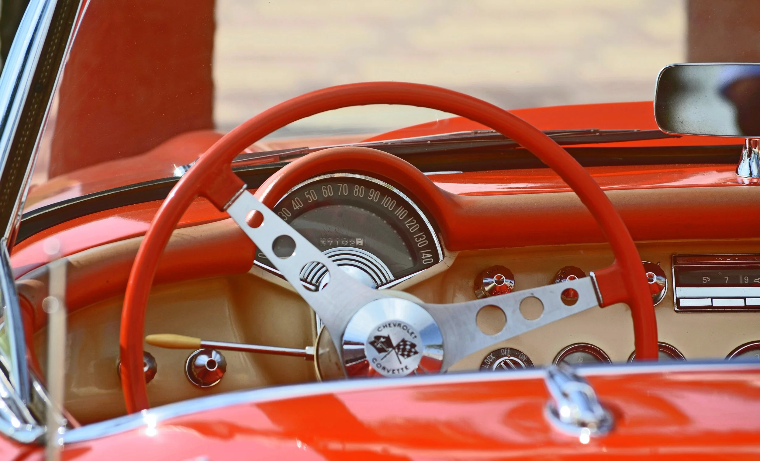 Close-up of the dashboard and steering wheel of a vintage red Chevrolet Corvette car, featuring a speedometer and various controls.