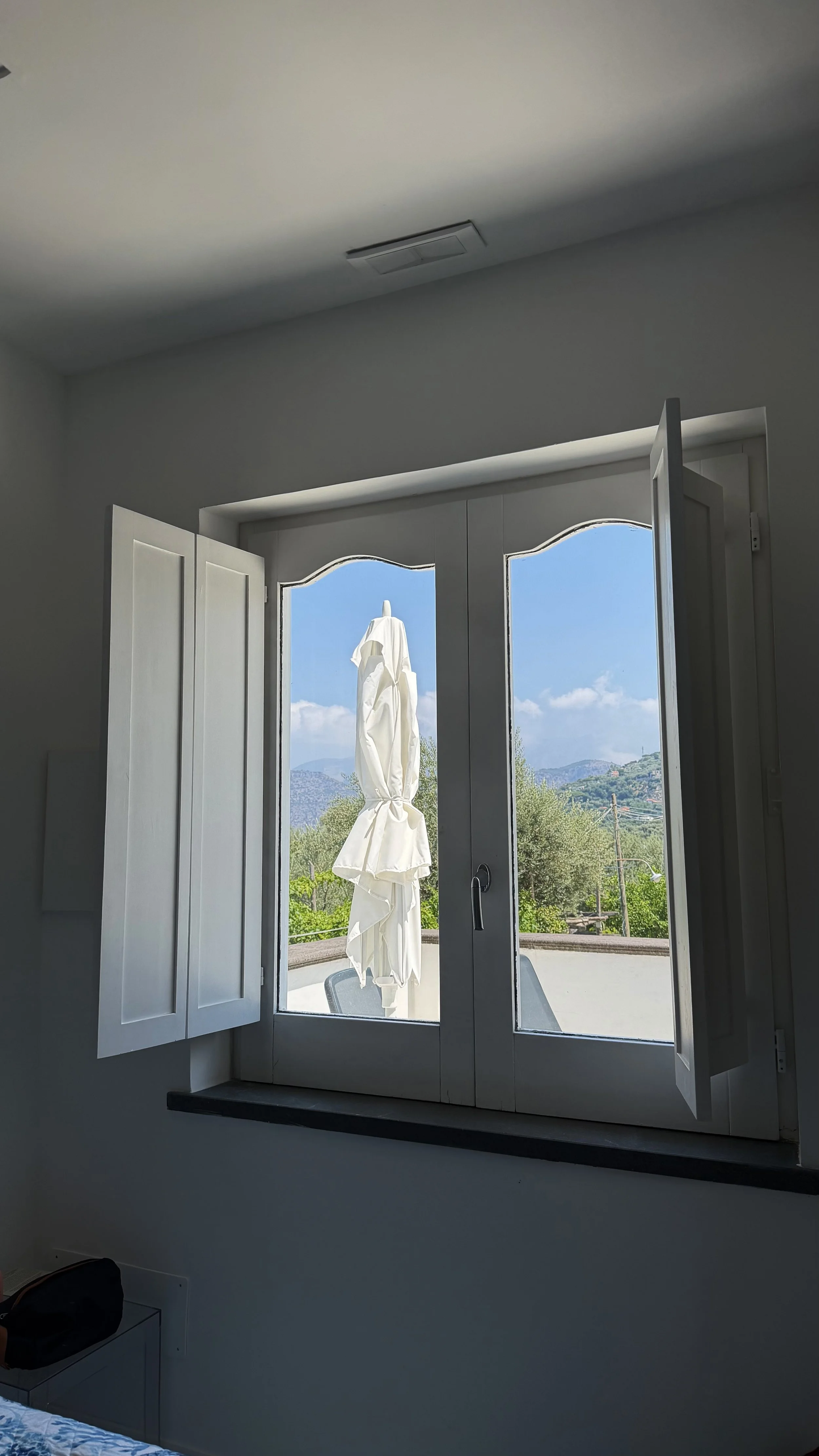 Interior view of open French doors with a white patio umbrella, blue sky, and mountainous landscape outside