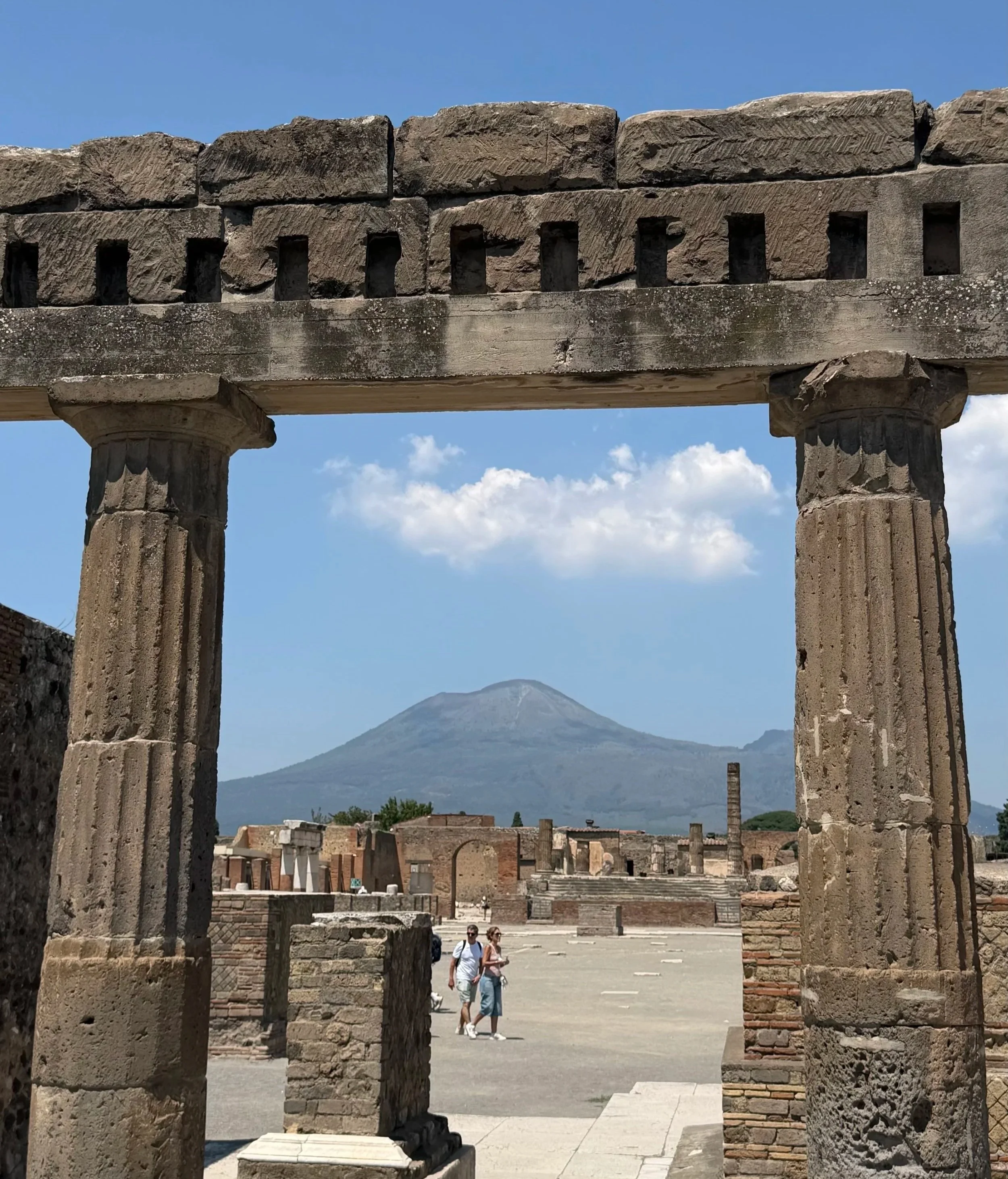 Ancient Pompeii ruins framed by stone columns, with Mount Vesuvius in the background
