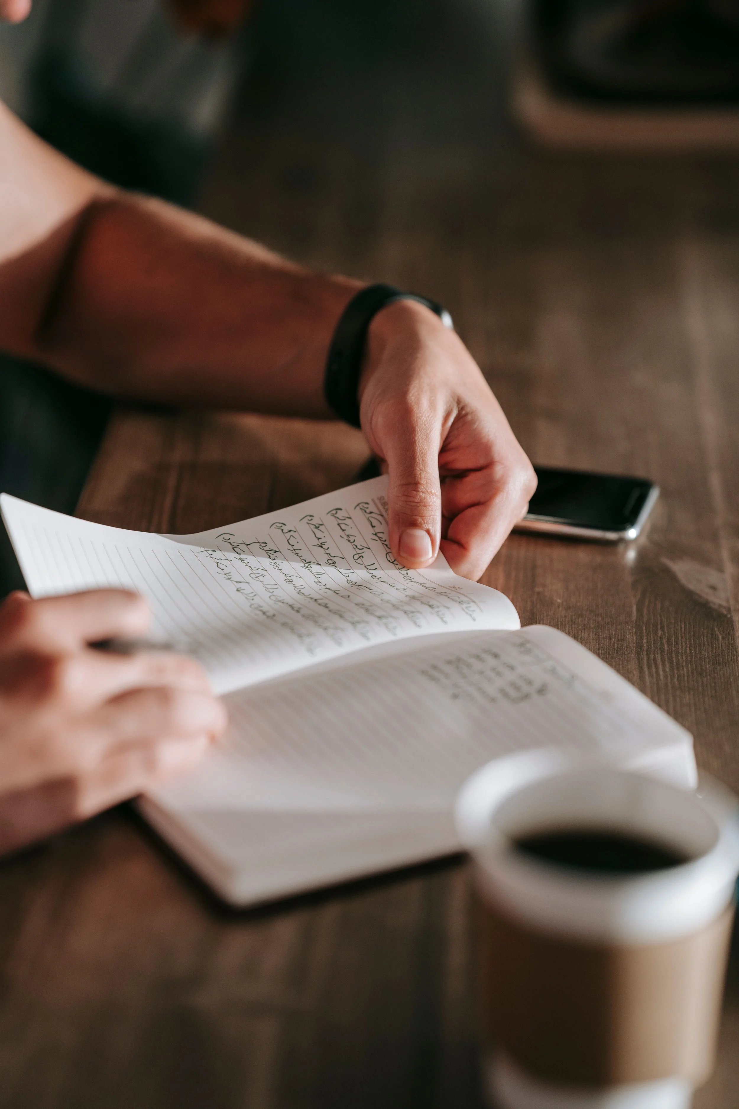 writing in notebook with pen to paper on wooden table with coffee