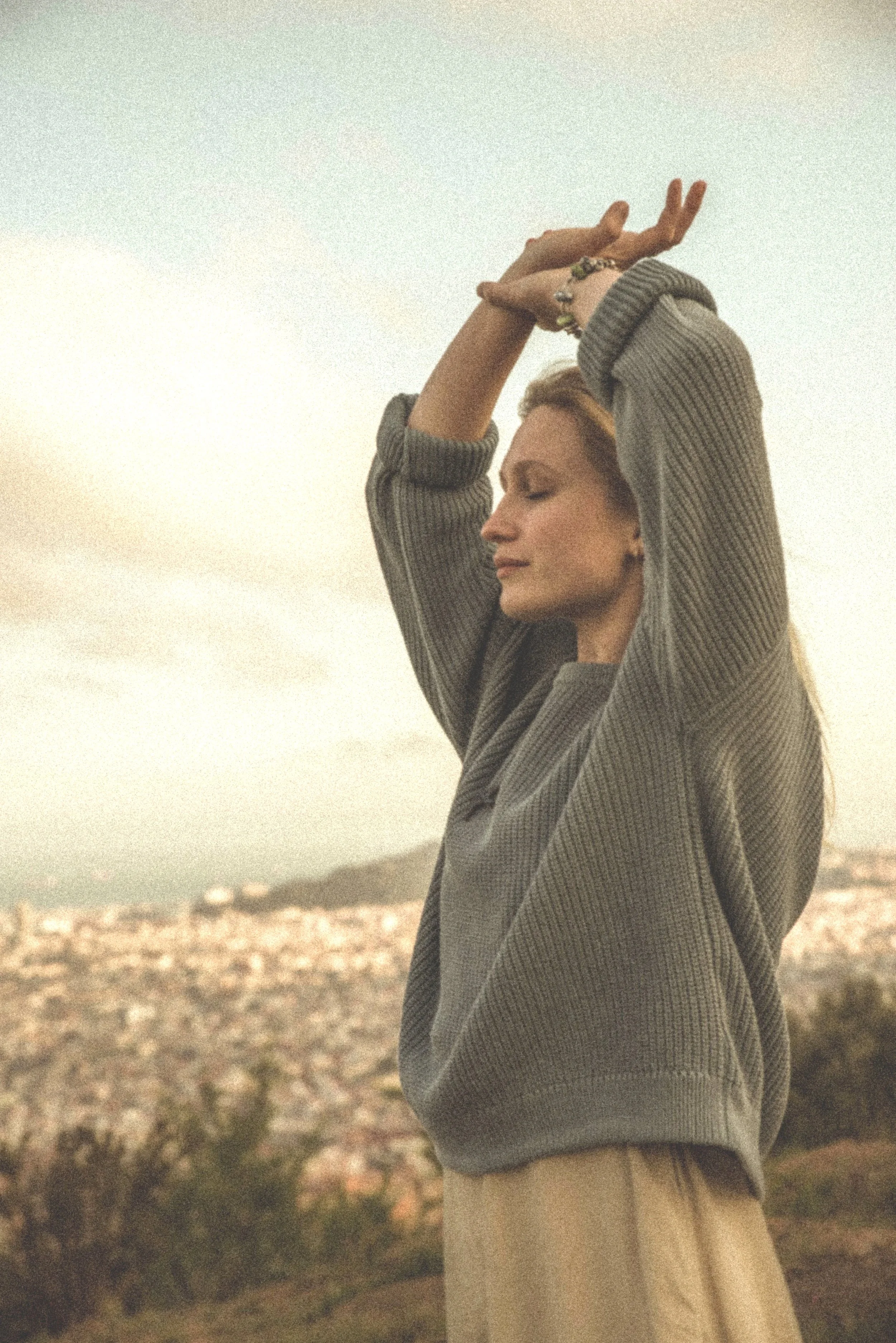 attractive female eye closed, arms over head overlooking city