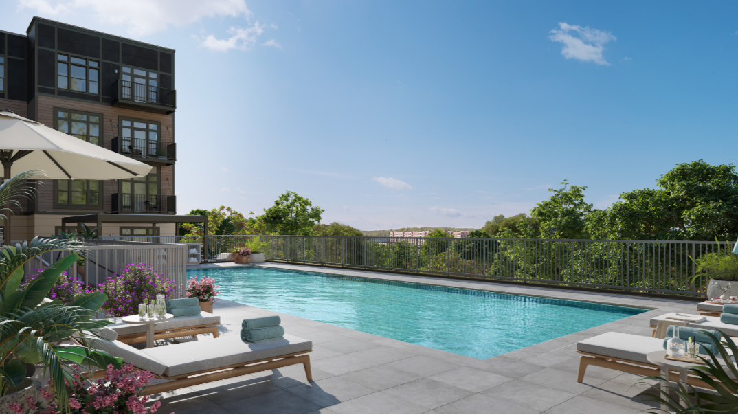 Outdoor swimming pool surrounded by lounge chairs, plants, and a modern apartment building in the background under a blue sky.