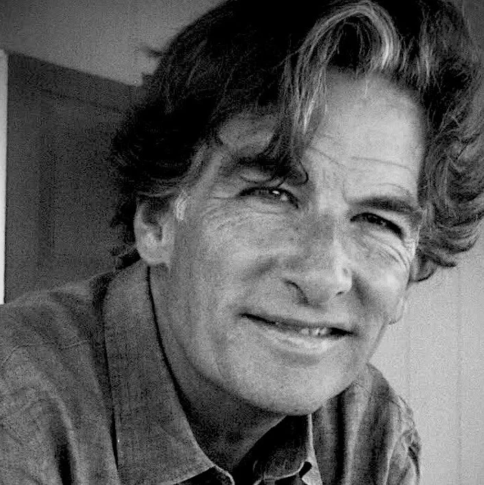 Black and white photo of a middle-aged man with wavy hair, smiling and wearing a collared shirt.