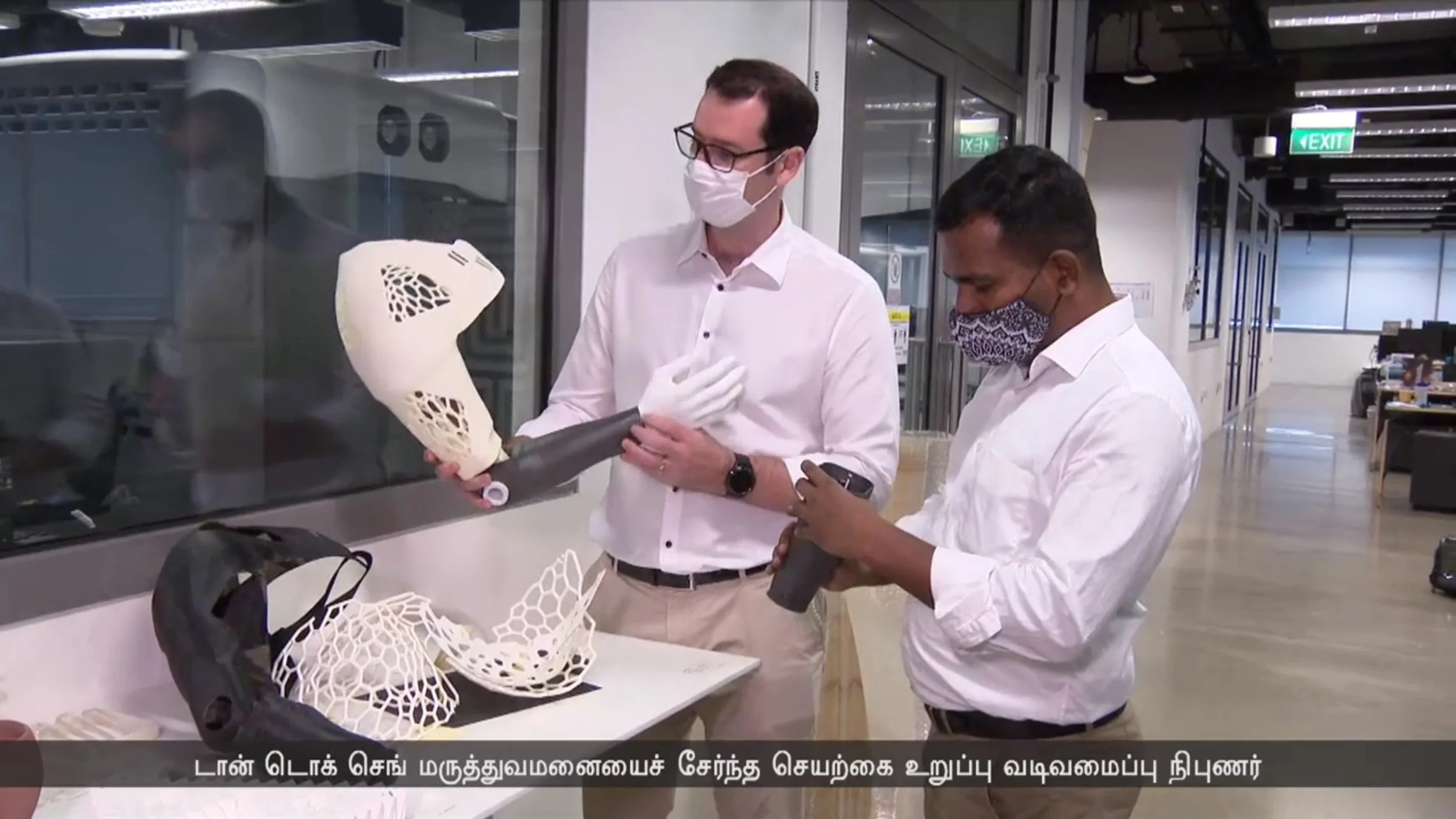Two men in white shirts and face masks inspecting and handling 3D-printed objects in a modern laboratory or industrial setting.