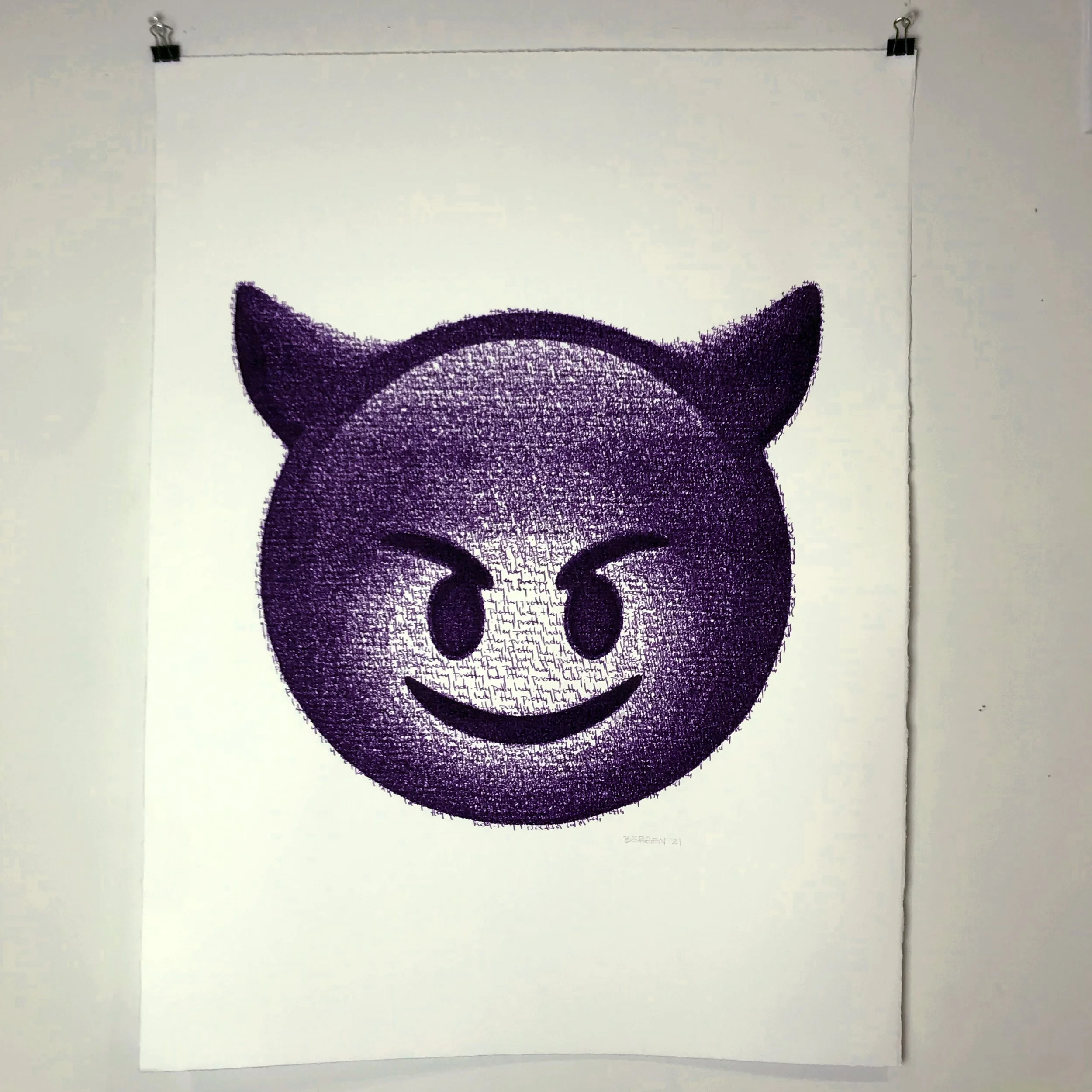 A white sheet of paper with a black and purple drawing of a cartoon cat face, attached to a wall with binder clips at the top corners.