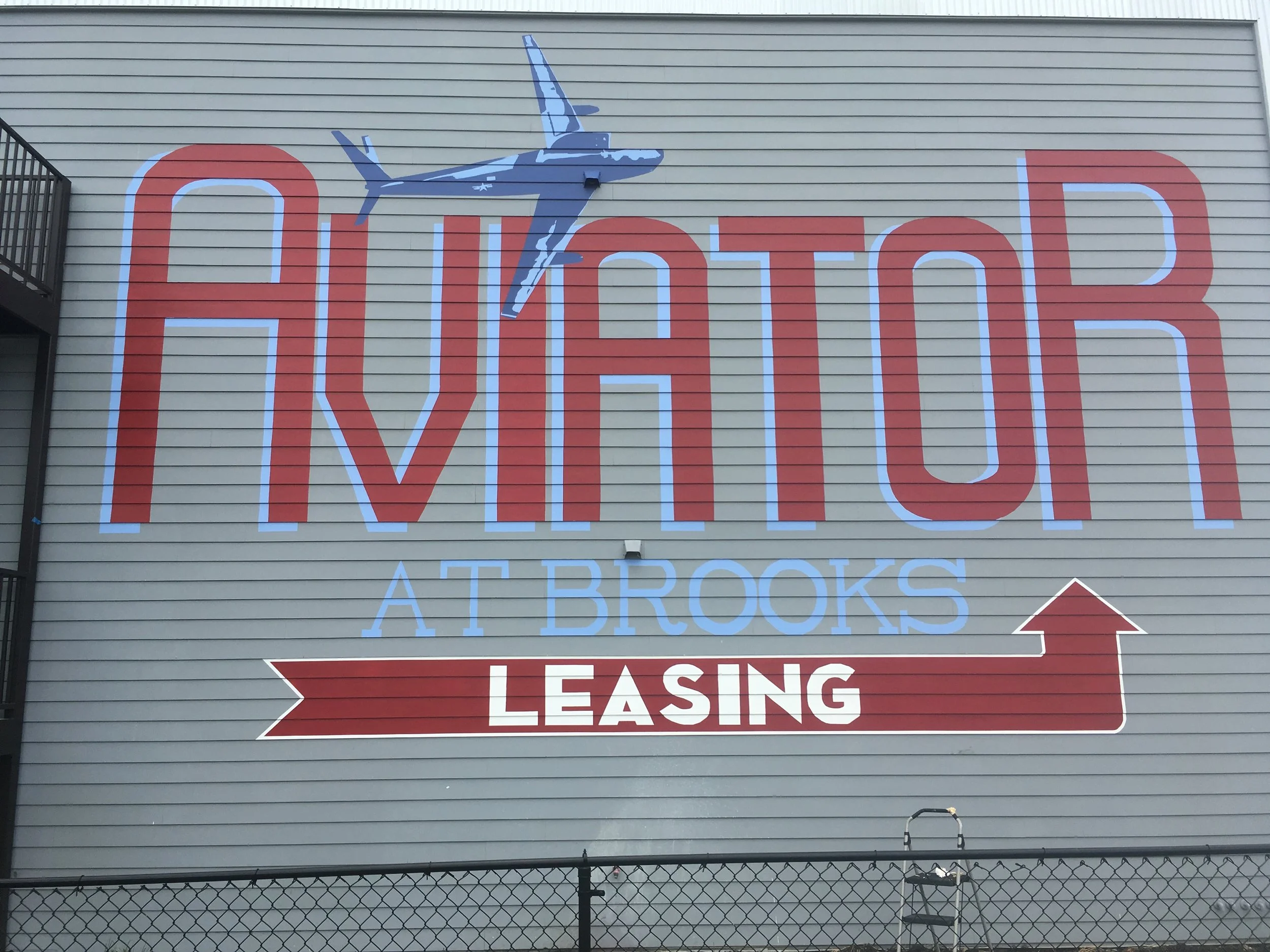 Sign on a building wall with a large red and white text that reads 'Arrow' and an airplane graphic above it. Below, there is a red and white directional arrow and the word 'Leasing'.