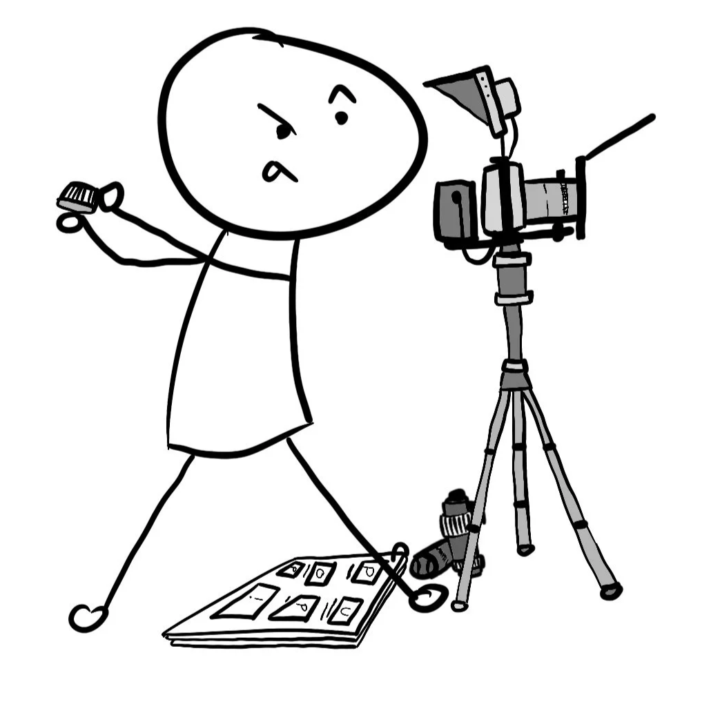Drawing of a stick figure person with an angry expression, holding a camera in one hand and a small object in the other, standing next to a camera on a tripod and a photo album on the floor.