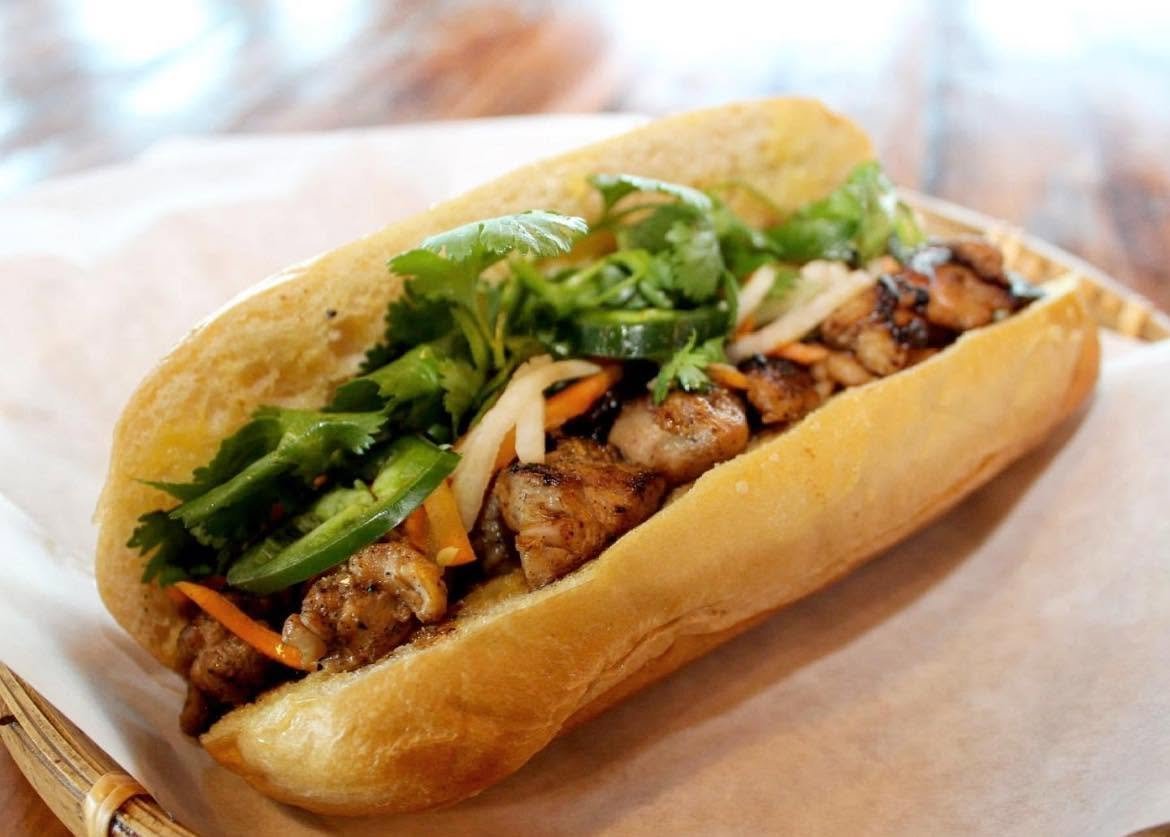 A Vietnamese banh mi sandwich with grilled meat, fresh cilantro, cucumbers, carrots, and pickled vegetables in a French baguette.