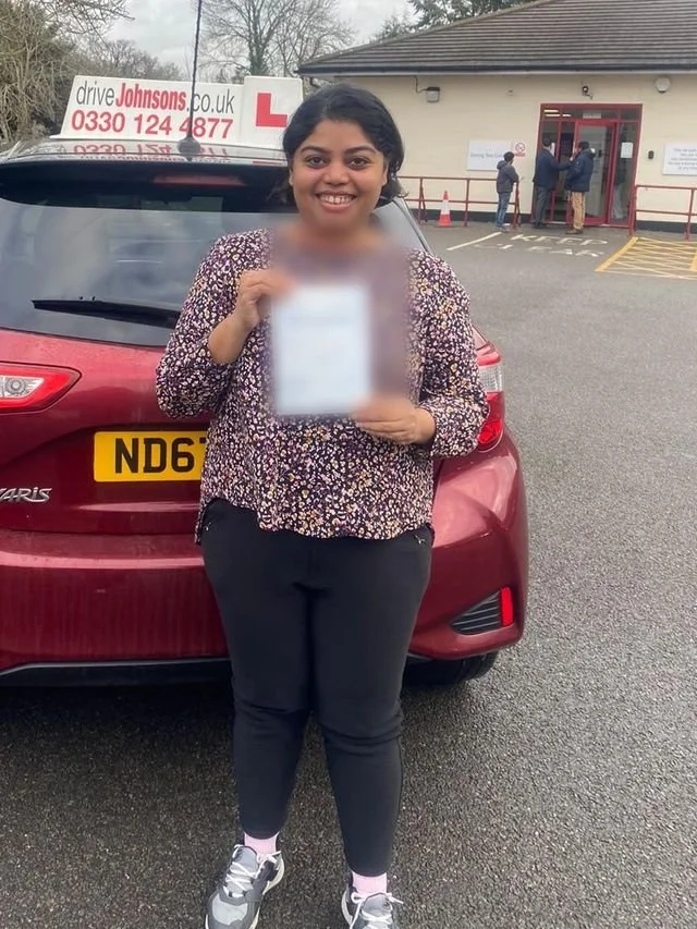 A student holding their driving test pass certificate beside the red Toyota Yaris