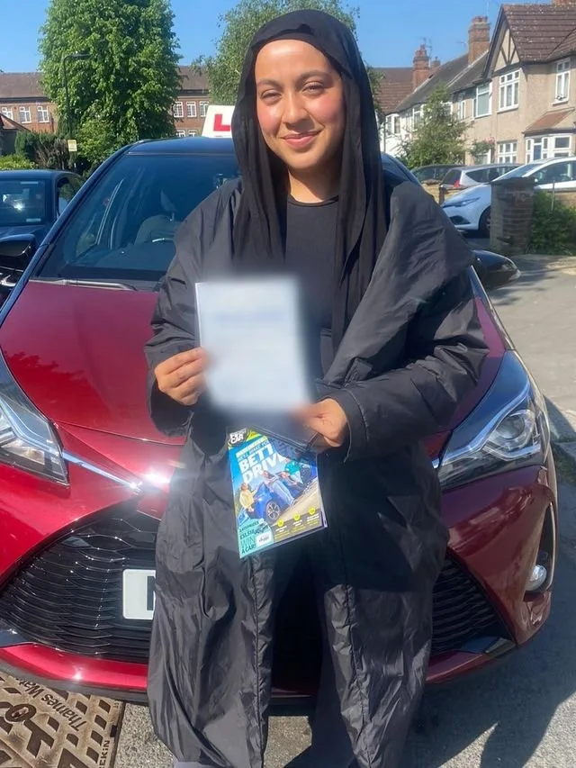 A student holding their driving test pass certificate beside the red Toyota Yaris