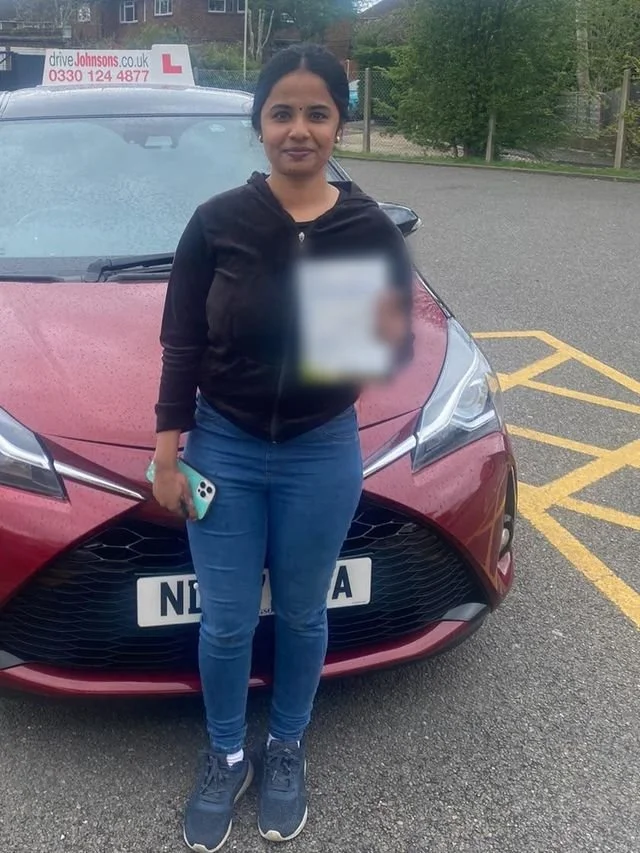 A student holding their driving test pass certificate beside the red Toyota Yaris