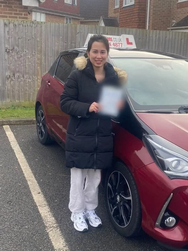 A student holding their driving test pass certificate beside the red Toyota Yaris