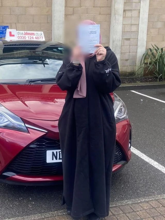 A student holding their pass certificate up in front of their face