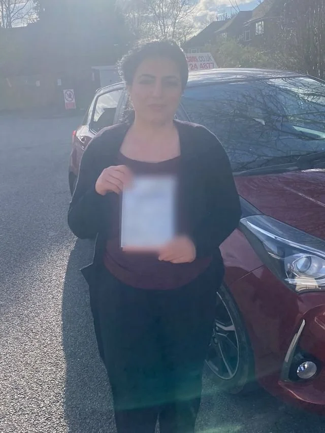 A student holding their driving test pass certificate beside the red Toyota Yaris