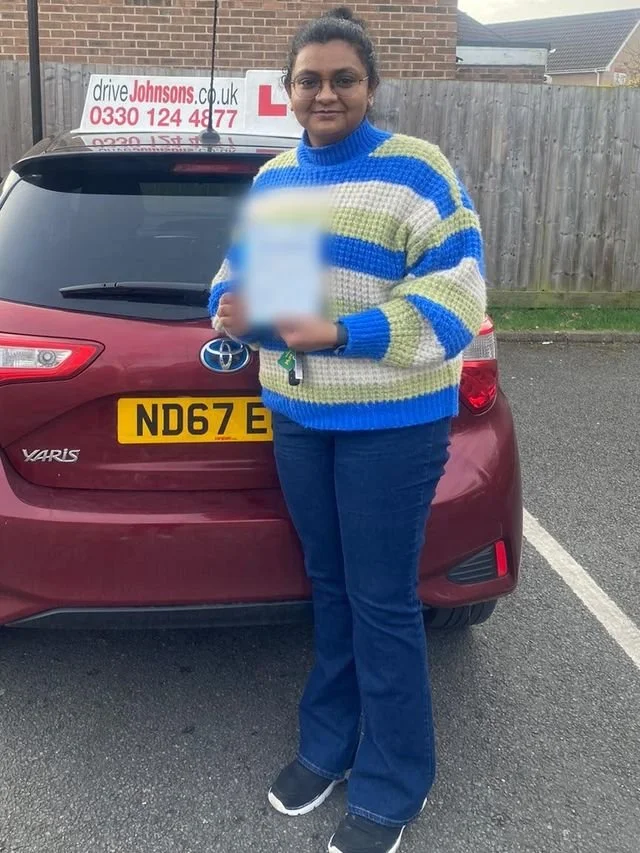 A student holding their driving test pass certificate beside the red Toyota Yaris