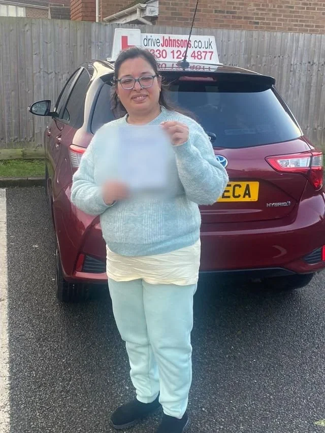 A student holding their driving test pass certificate beside the red Toyota Yaris
