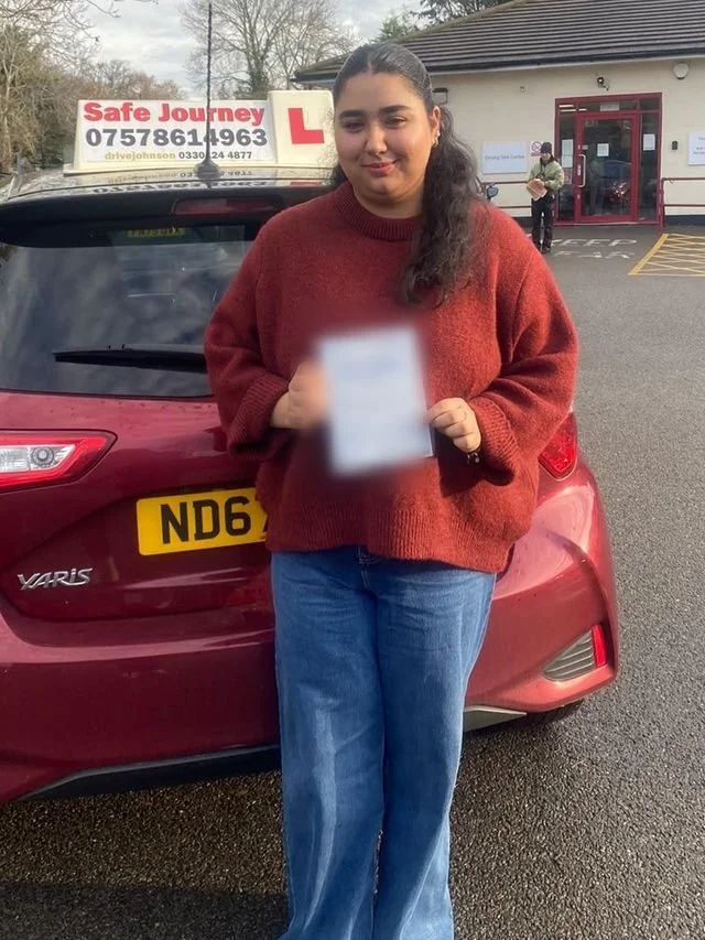 A student holding their driving test pass certificate beside the red Toyota Yaris