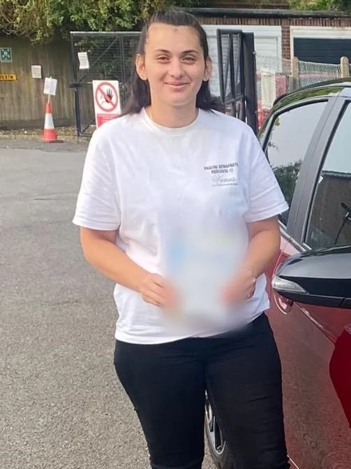 A student holding their driving test pass certificate beside the red Toyota Yaris