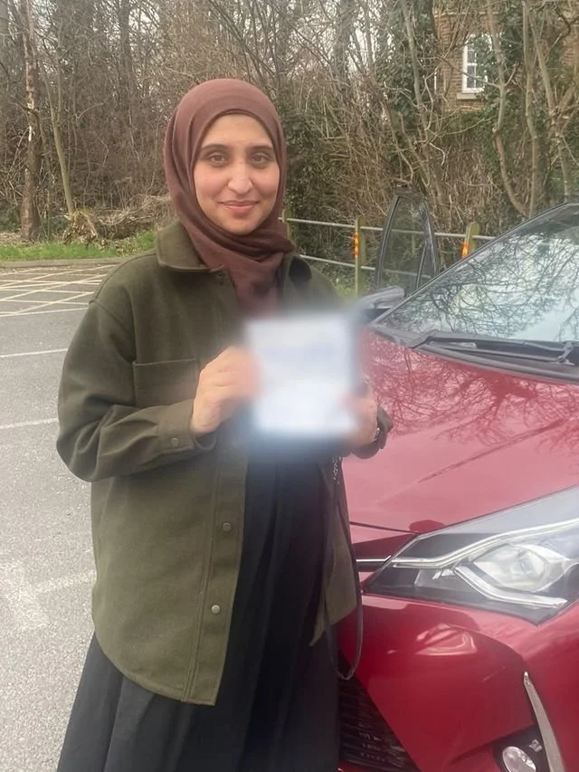 A student holding their driving test pass certificate beside the red Toyota Yaris