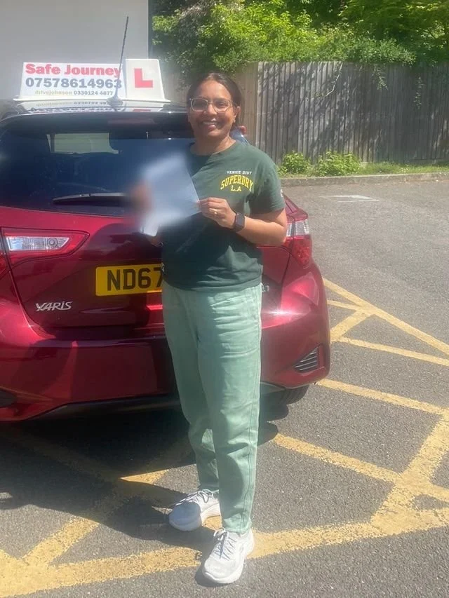 A student holding their driving test pass certificate beside the red Toyota Yaris