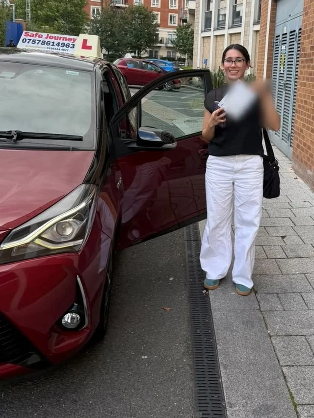 A student holding their driving test pass certificate beside the red Toyota Yaris