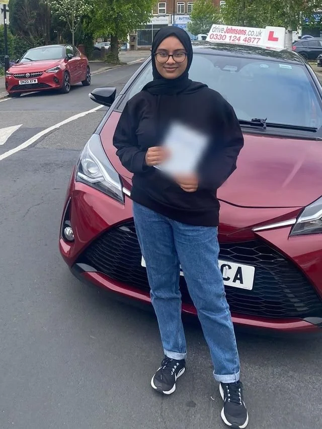 A student holding their driving test pass certificate beside the red Toyota Yaris