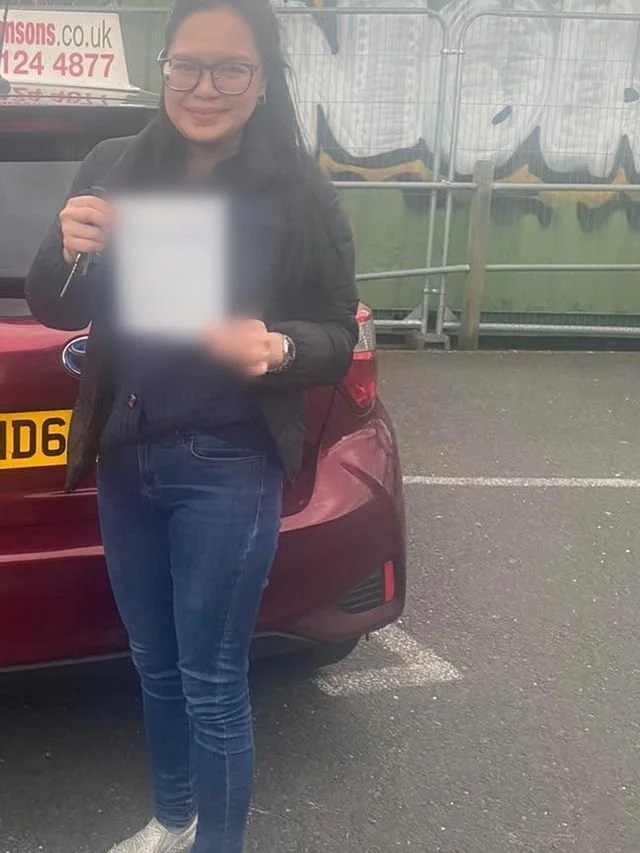 A student holding their driving test pass certificate beside the red Toyota Yaris