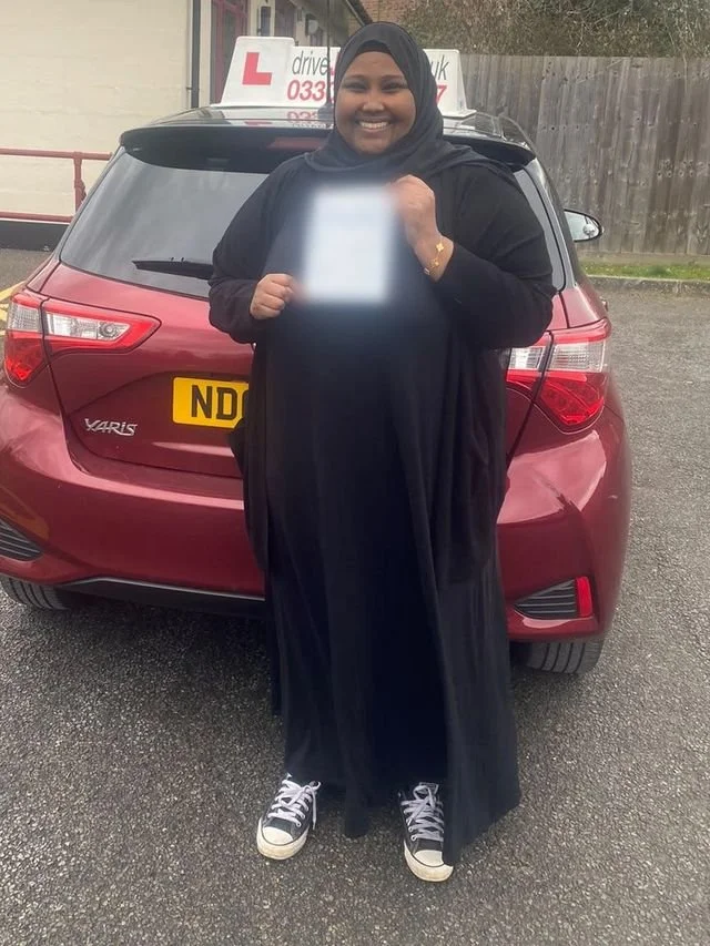 A student holding their driving test pass certificate beside the red Toyota Yaris