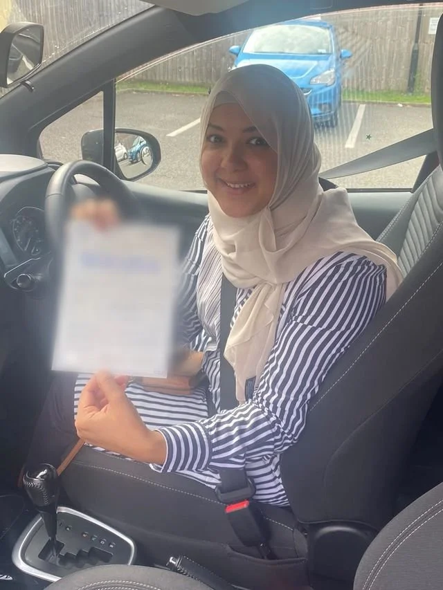 A student in the driver’s seat holding their driving test pass certificate