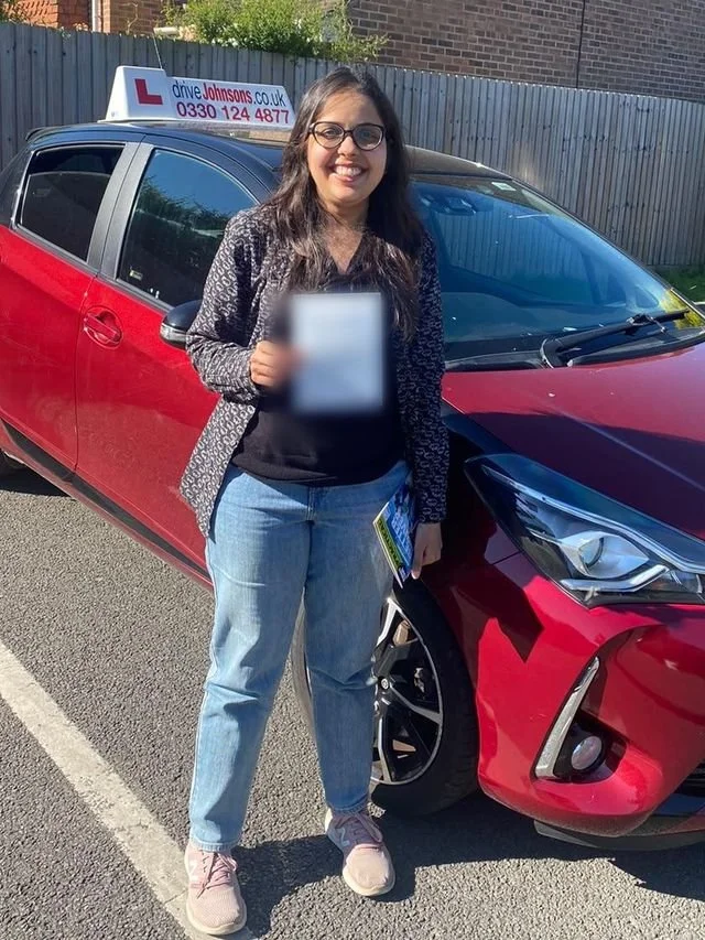 A student holding their driving test pass certificate beside the red Toyota Yaris