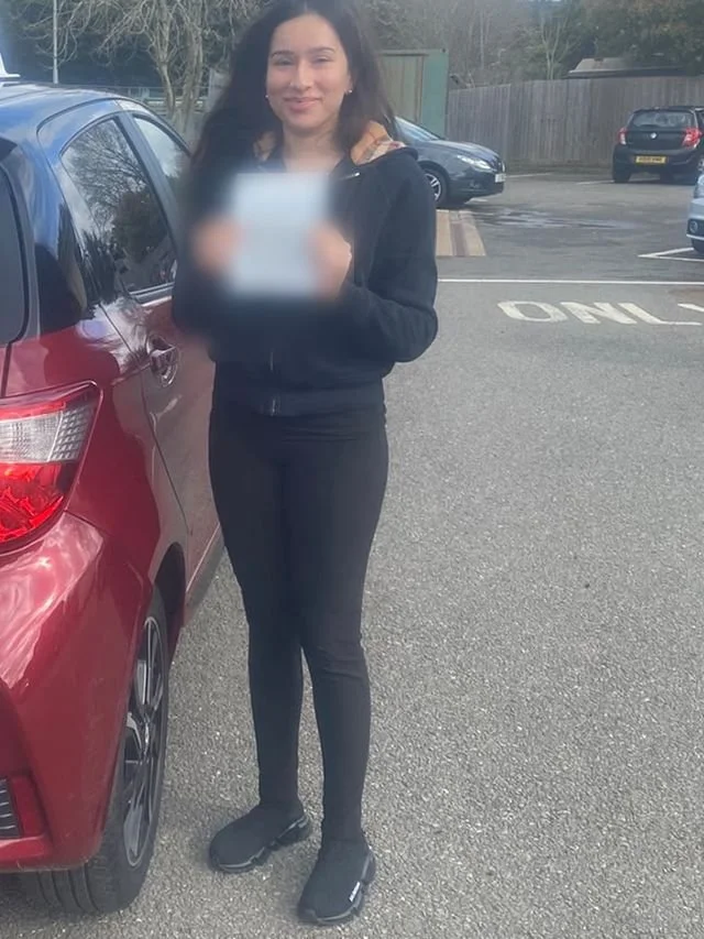 A student holding their driving test pass certificate beside the red Toyota Yaris