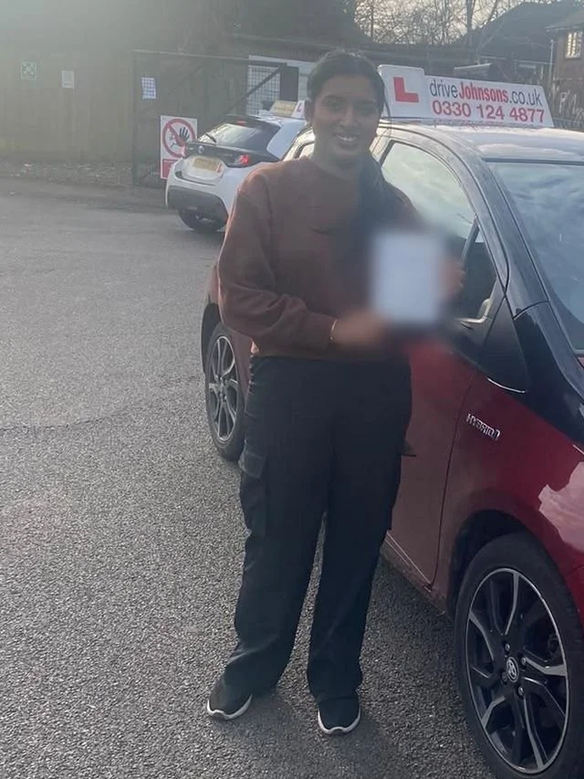 A student holding their driving test pass certificate beside the red Toyota Yaris