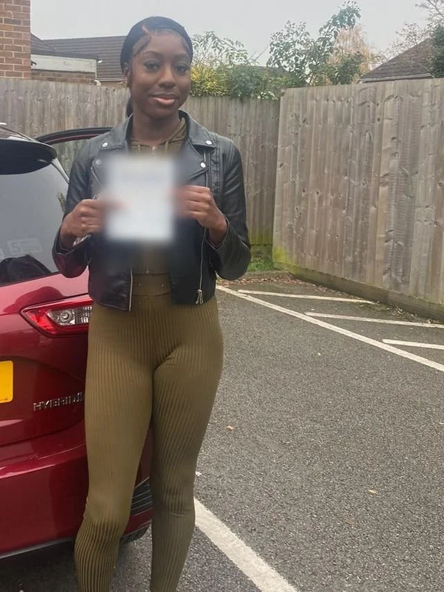 A student holding their driving test pass certificate beside the red Toyota Yaris