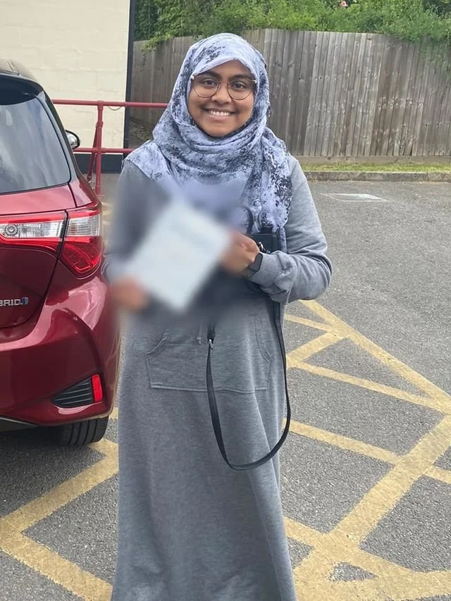 A student holding their driving test pass certificate beside the red Toyota Yaris