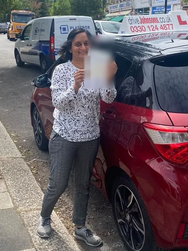 A student holding their driving test pass certificate beside the red Toyota Yaris
