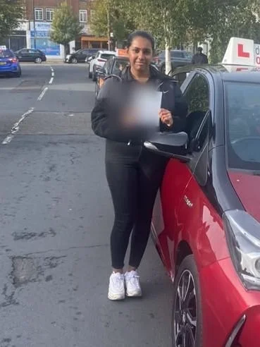 A student holding their driving test pass certificate beside the red Toyota Yaris