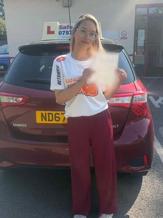 A student holding their driving test pass certificate beside the red Toyota Yaris