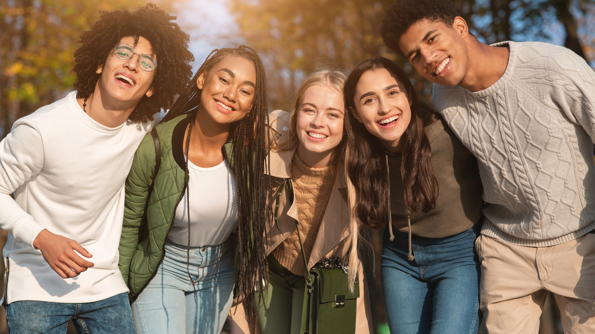 Six young adults standing outdoors in fall, smiling at the camera.