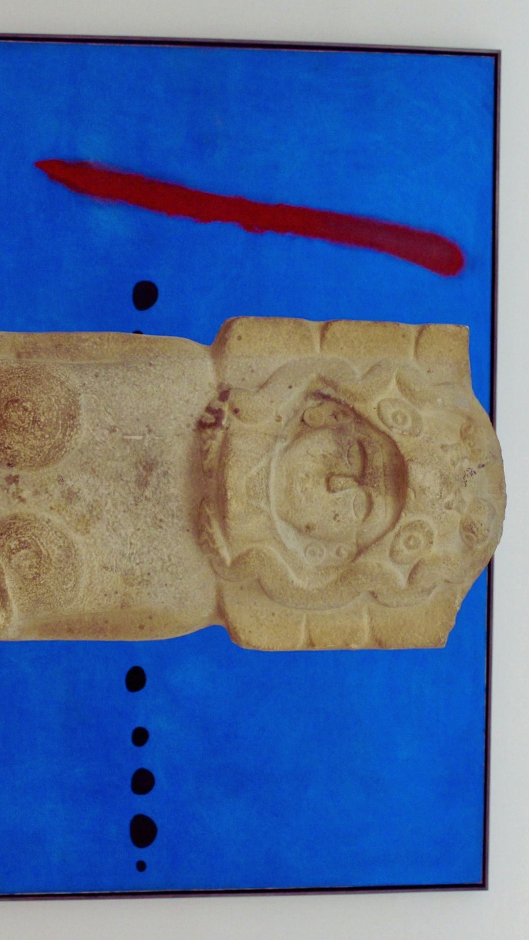 An ancient carved stone statue of a mesoamerican goddess, placed in front of Bleu II by Juan Miró.